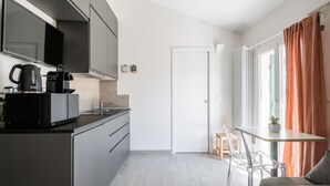 A modern kitchen with a coffee maker, microwave, and kettle. There is a dining area with a table and chairs.