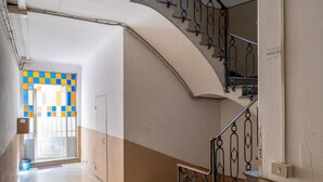 A hallway with a curved staircase, a door with a colorful checkered pattern, and a light fixture on the ceiling.