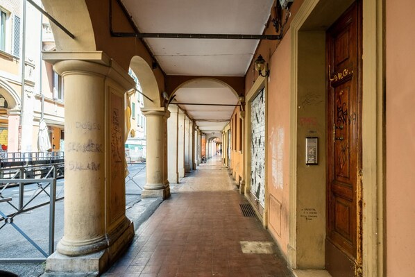 A corridor with columns, a tiled floor, and a wooden door with graffiti. - Appartamento all Orto Botanico by Wonderful Italy (Bologna)