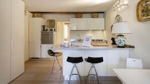 A modern kitchen with white cabinets, a central island with stools, a stove, and a microwave. - Nel Cuore del Borgo di Camogli by Wonderful Italy (Camogli)