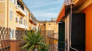 A narrow outdoor corridor with a potted plant, a black refrigerator, and a metal fence. - Studio Malcontenti con Terrazzo by Wonderful Italy (Bologna)