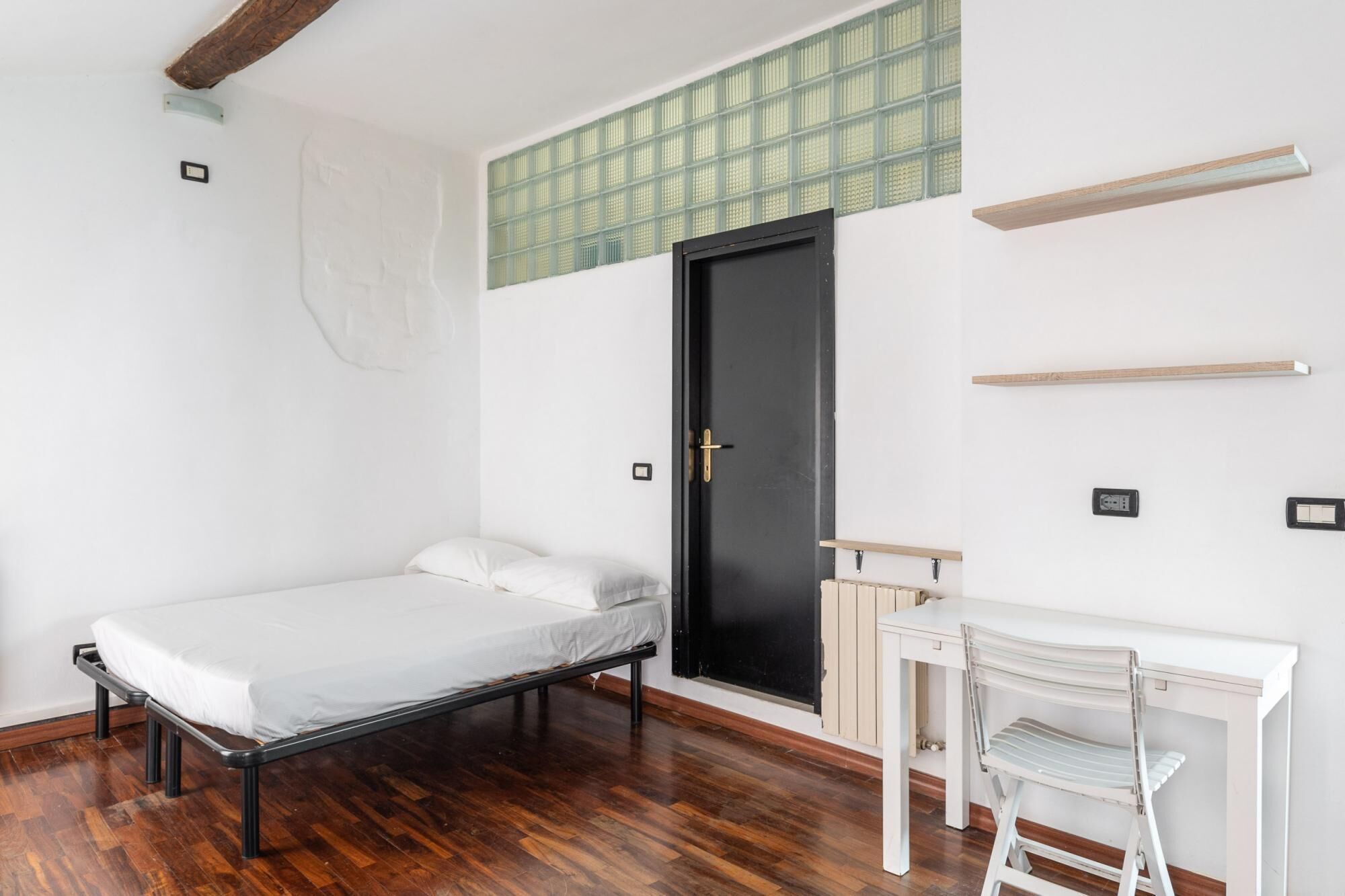 A minimalist room with a bed, a desk, and a black door.