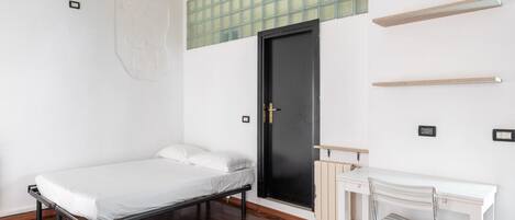 A minimalist room with a bed, a desk, and a black door.