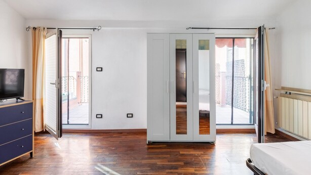 A room with a wooden floor, a bed, a TV on a dresser, and a sliding door leading to an outdoor area. - Studio Malcontenti con Terrazzo by Wonderful Italy (Bologna)