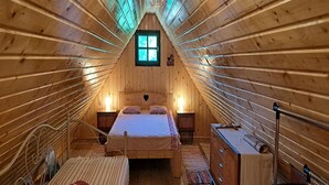 Ein gemütliches Schlafzimmer im Dachgeschoss mit Bett, zwei Nachttischlampen, einem kleinen Fenster und einer Holzkommode.