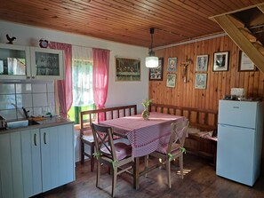 A cozy kitchen with wooden cabinets, a dining table with checkered tablecloth, and a refrigerator.