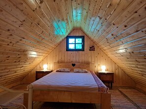 A cozy attic bedroom with a sloped ceiling, a bed with a patterned bedspread, two bedside lamps, and a window with a view.