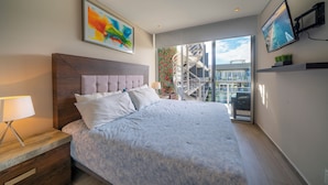 Une chambre moderne avec un grand lit, une table de chevet, une télévision et un balcon offrant une vue sur la ville.