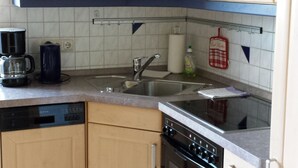 Eine kompakte Küche mit Holzausstattung, einem Geschirrspüler, einem Backofen und einer Kaffeemaschine.