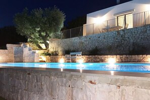 A stone wall with a pool and a white building with a balcony.