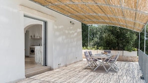 A covered patio area with a table and chairs, a kitchen visible through an open door, and a bamboo ceiling. - Villa Degli Ulivi con Piscina by Wonderful Italy (Ostuni)