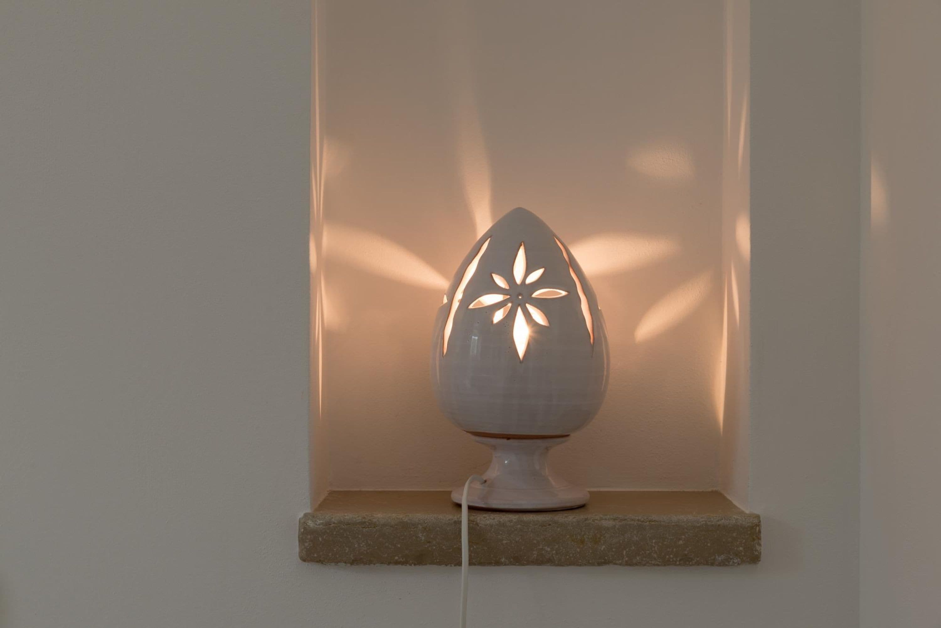 A white, egg-shaped lamp with a floral design on a stone shelf against a plain wall.