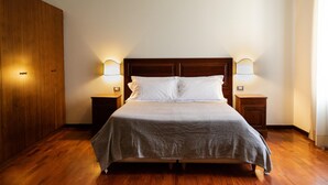 A neatly made bed with a wooden headboard, two bedside tables with lamps, and a wooden wardrobe. - Agatea a due Passi dal Duomo by Wonderful Italy (Catania)