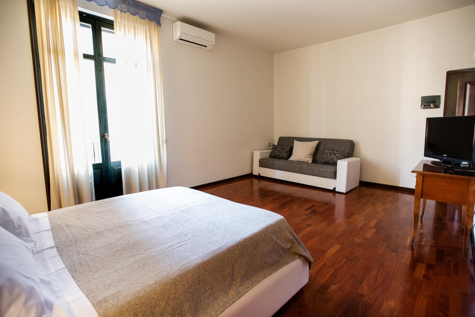 A hotel room with a bed, a sofa, a TV, and a wooden floor.