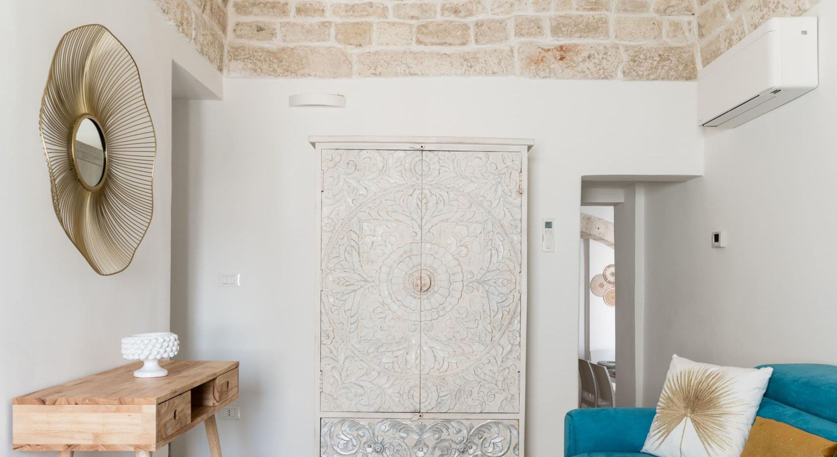 A room with a stone ceiling, a decorative mirror, a wardrobe with intricate designs, and a blue sofa with patterned cushions.