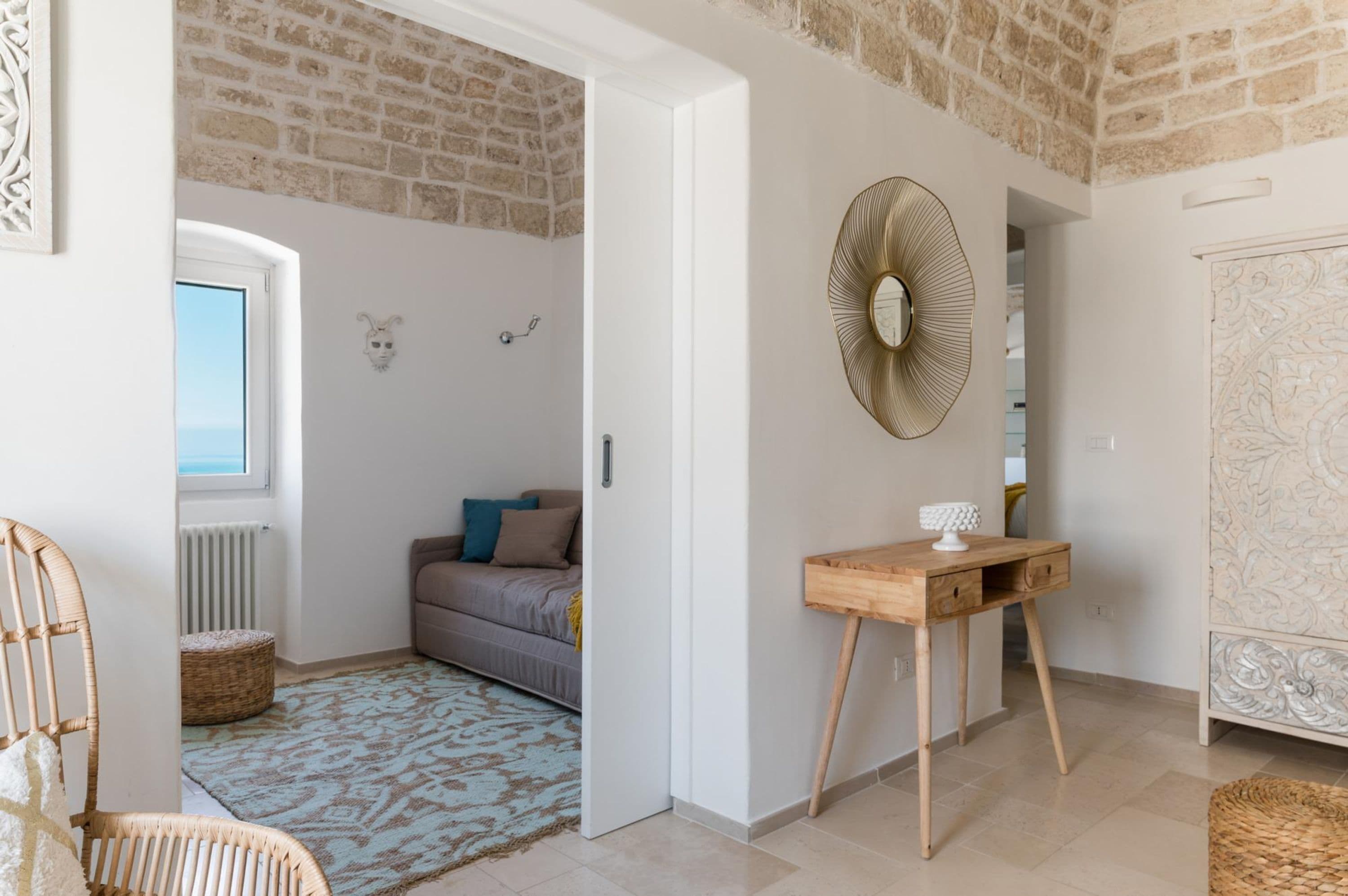 A room with a bed, a wooden console table, a decorative fan, and a rustic brick wall.