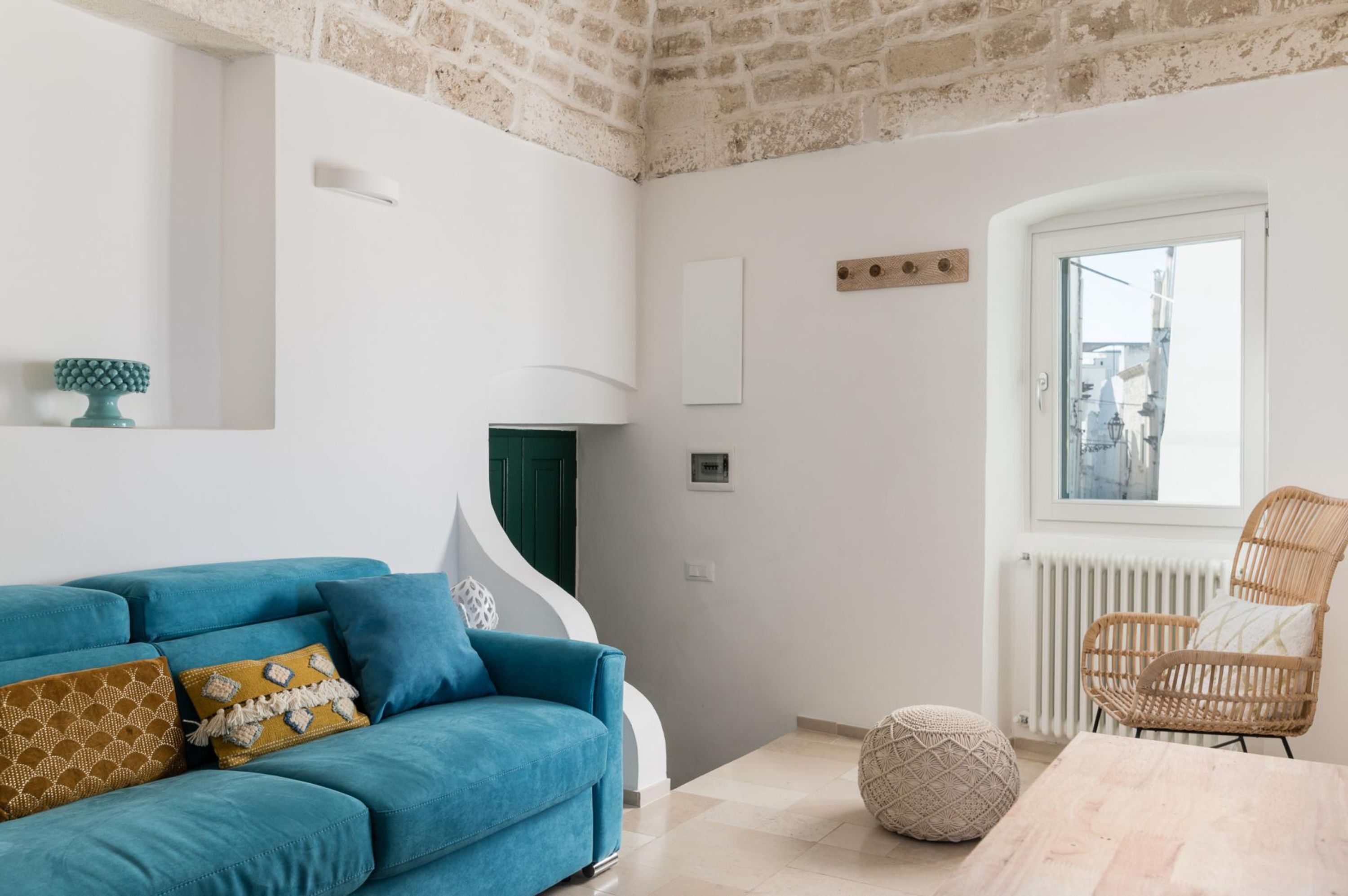 Una sala de estar moderna con un sofá azul, una silla de mimbre, una mesa de madera y vistas a través de una ventana.