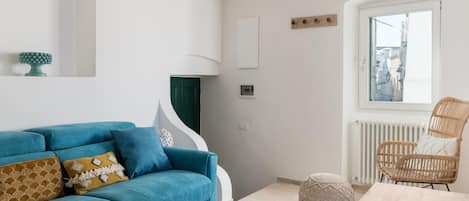 Una sala de estar moderna con un sofá azul, una silla de mimbre, una mesa de madera y vistas a través de una ventana.