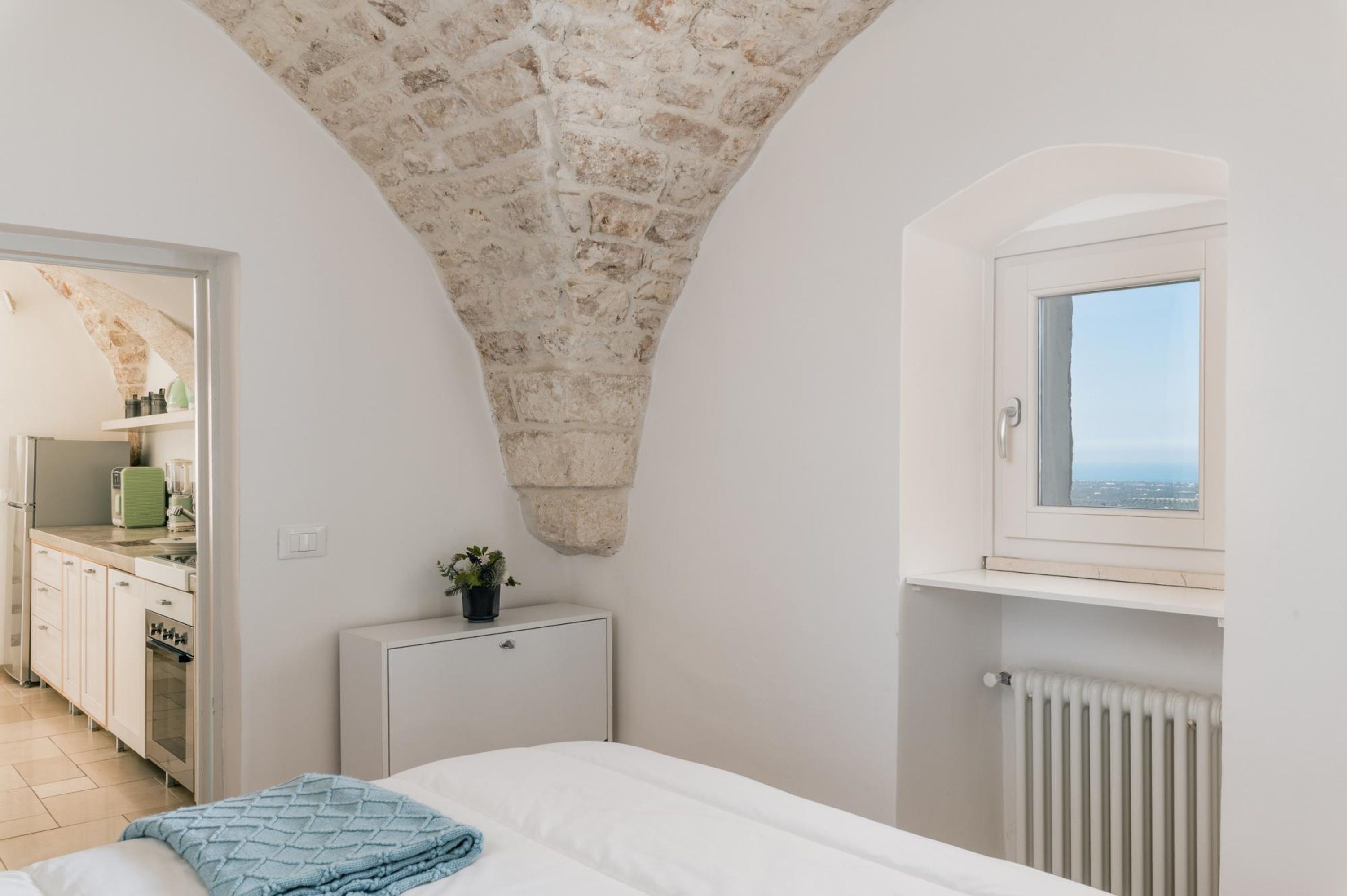 Une chambre avec un plafond en pierre, une fenêtre donnant sur un beau paysage, un lit et une petite armoire.
