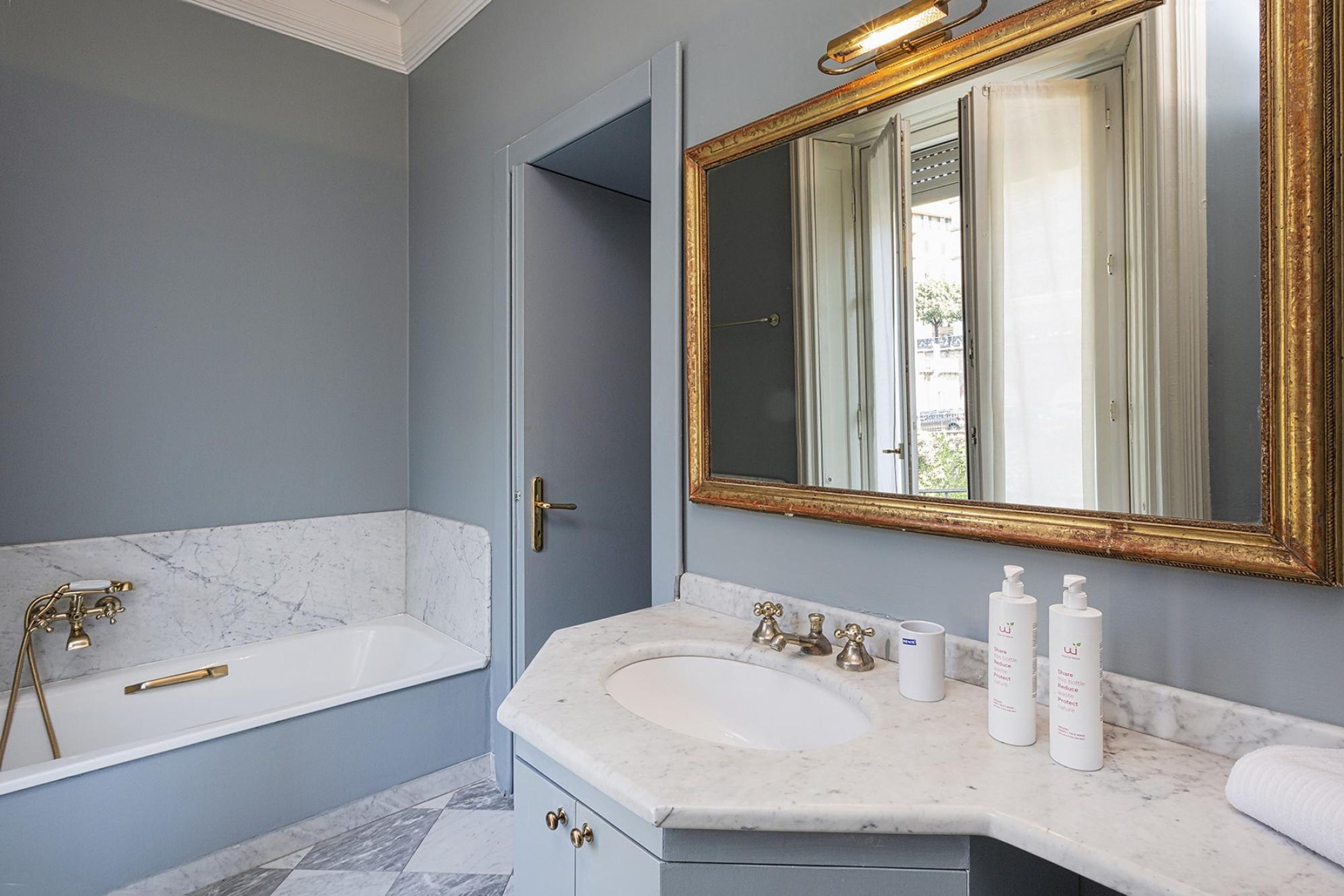 Une salle de bain avec une baignoire, un lavabo avec deux robinets et un grand miroir avec un cadre doré.