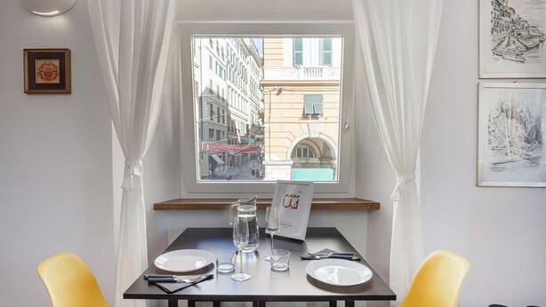 Una mesa de comedor con vista a una calle de la ciudad a través de una ventana, un cuadro en la pared y una tarjeta de menú sobre la mesa.
