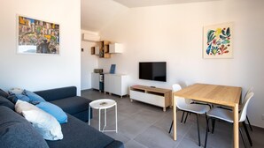 Un salon moderne avec un canapé, un téléviseur, une table à manger avec des chaises et des œuvres d’art accrochées aux murs.