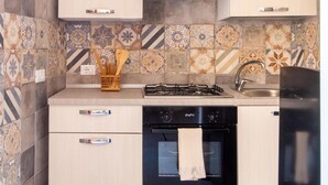Une cuisine compacte avec des meubles de couleur bois clair, une hotte de cuisine en acier inoxydable, un lave-vaisselle et un crédence en carreaux décoratifs.