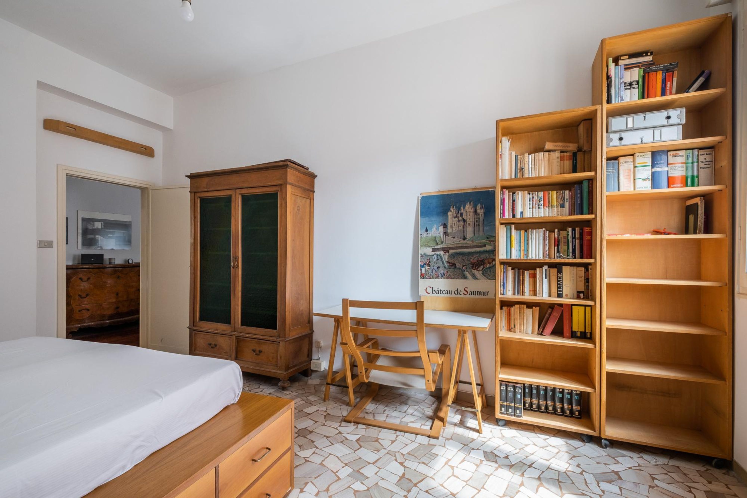 A bedroom with a bed, wooden desk, bookshelves, and a wardrobe.