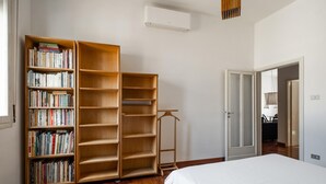 A bedroom with a large bookshelf filled with books, a bed with white bedding, and a wooden floor.