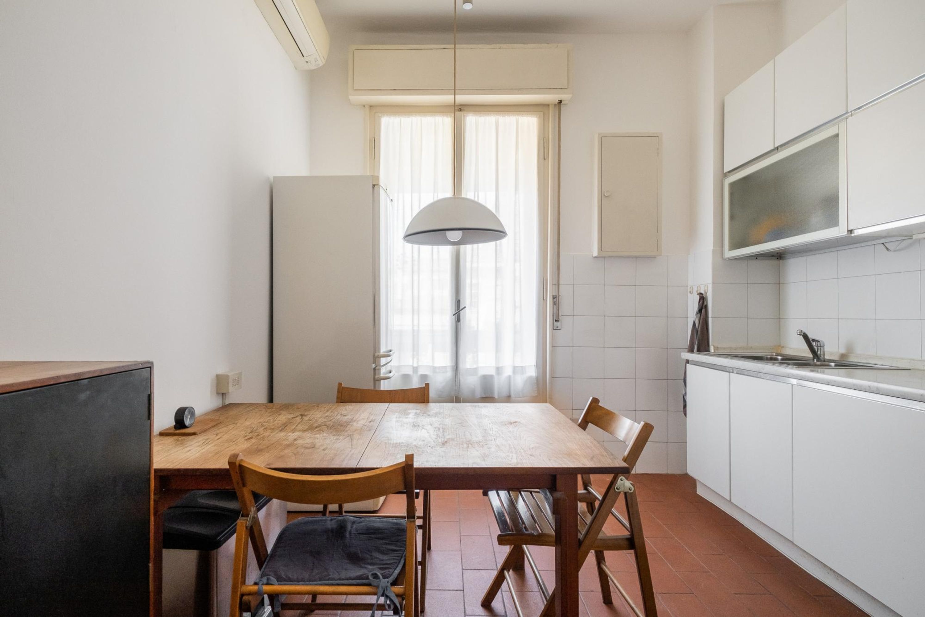 A compact kitchen with white cabinets, a wooden dining table, and a hanging light fixture.