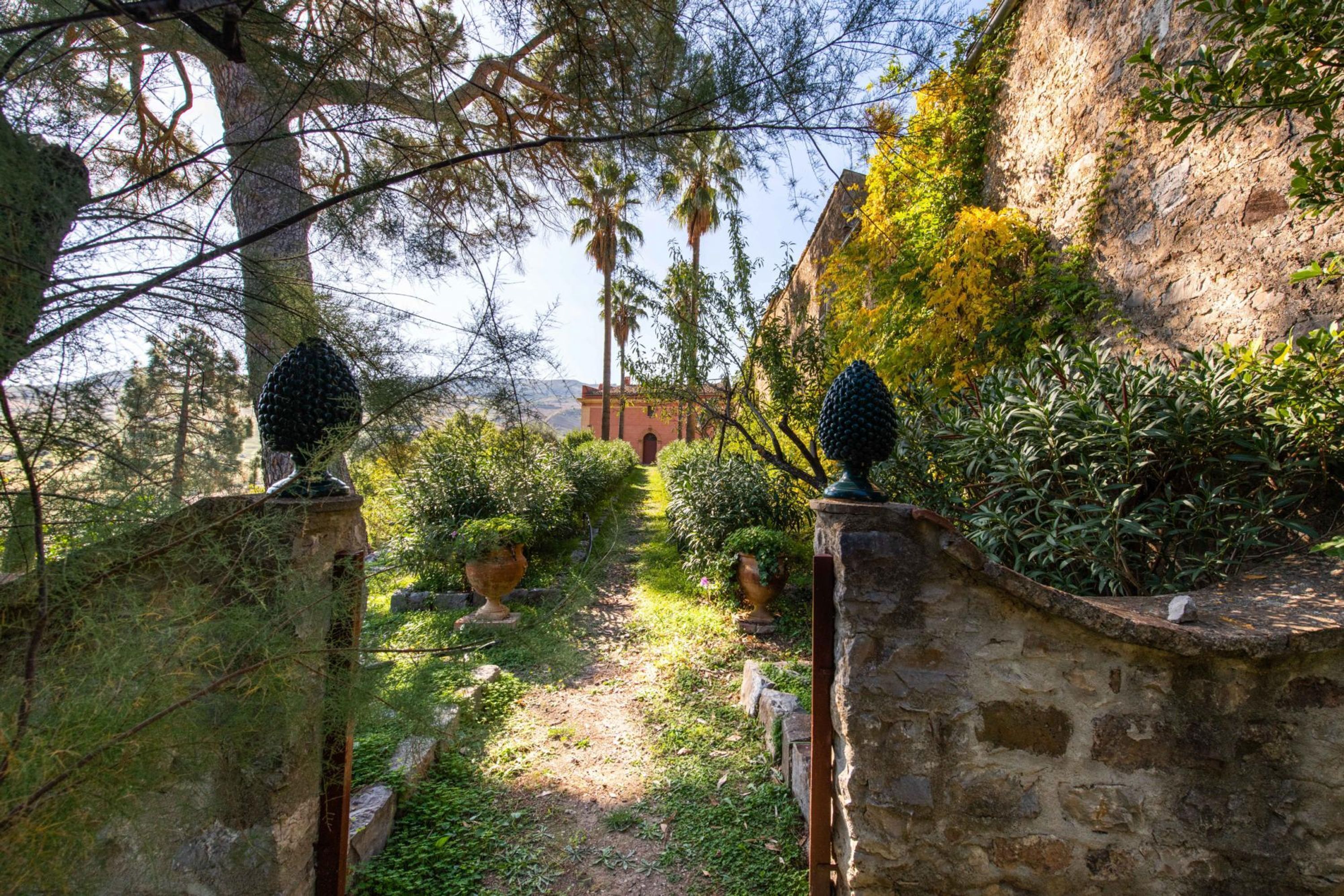 Un sendero de piedra que atraviesa un jardín con plantas en macetas y una vista de un edificio a lo lejos.