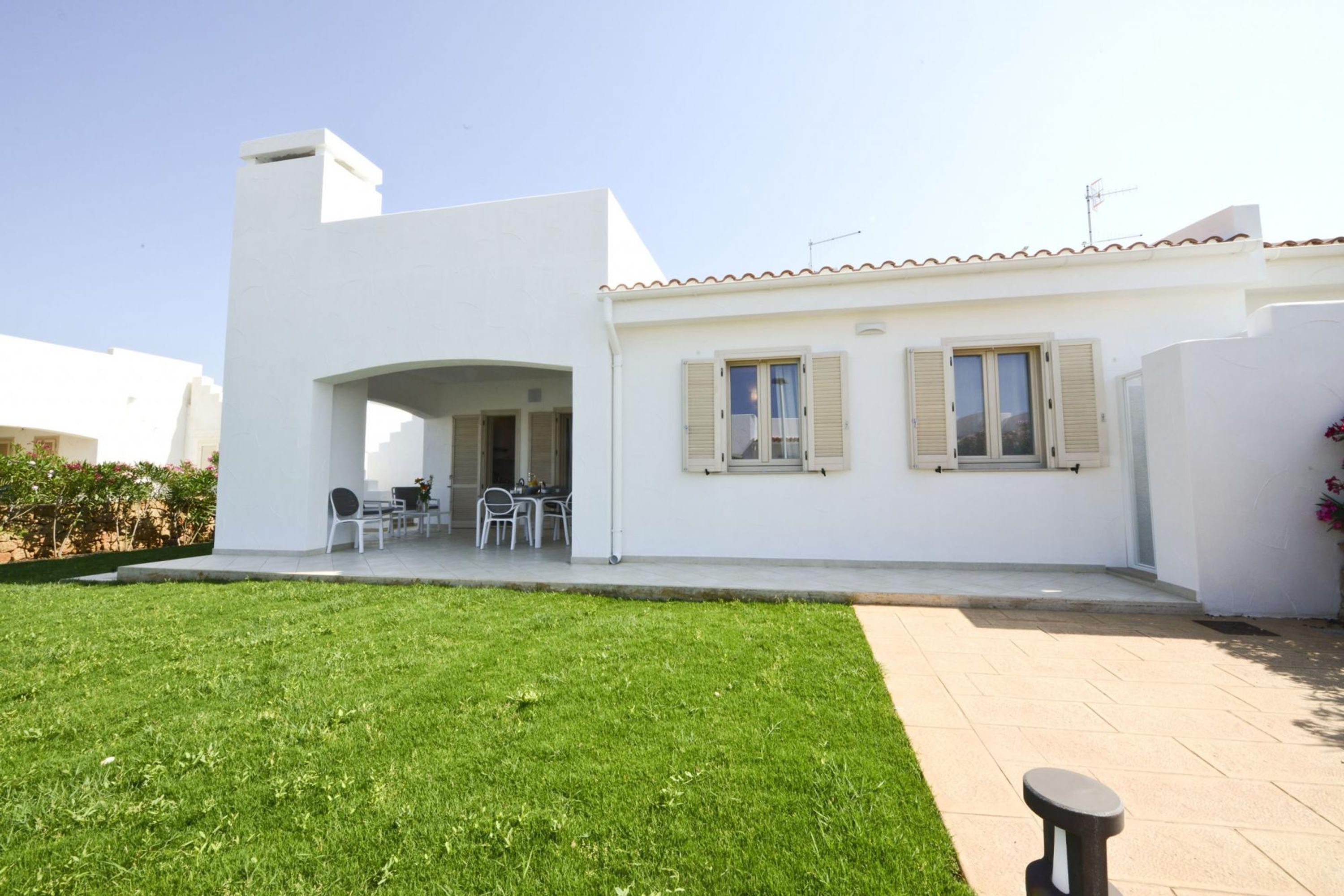 A white building with a tiled roof, a patio area with outdoor furniture, and a well-maintained lawn.