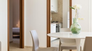 A modern dining area with a round table, white chairs, and a green vase with white flowers. - Charming Villa With Pool by Wonderful Italy (Ostuni)