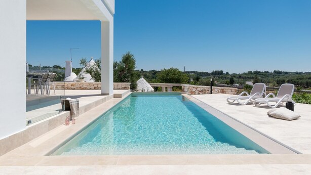 A swimming pool with lounge chairs and a stone structure in the background. - Charming Villa With Pool by Wonderful Italy (Ostuni)