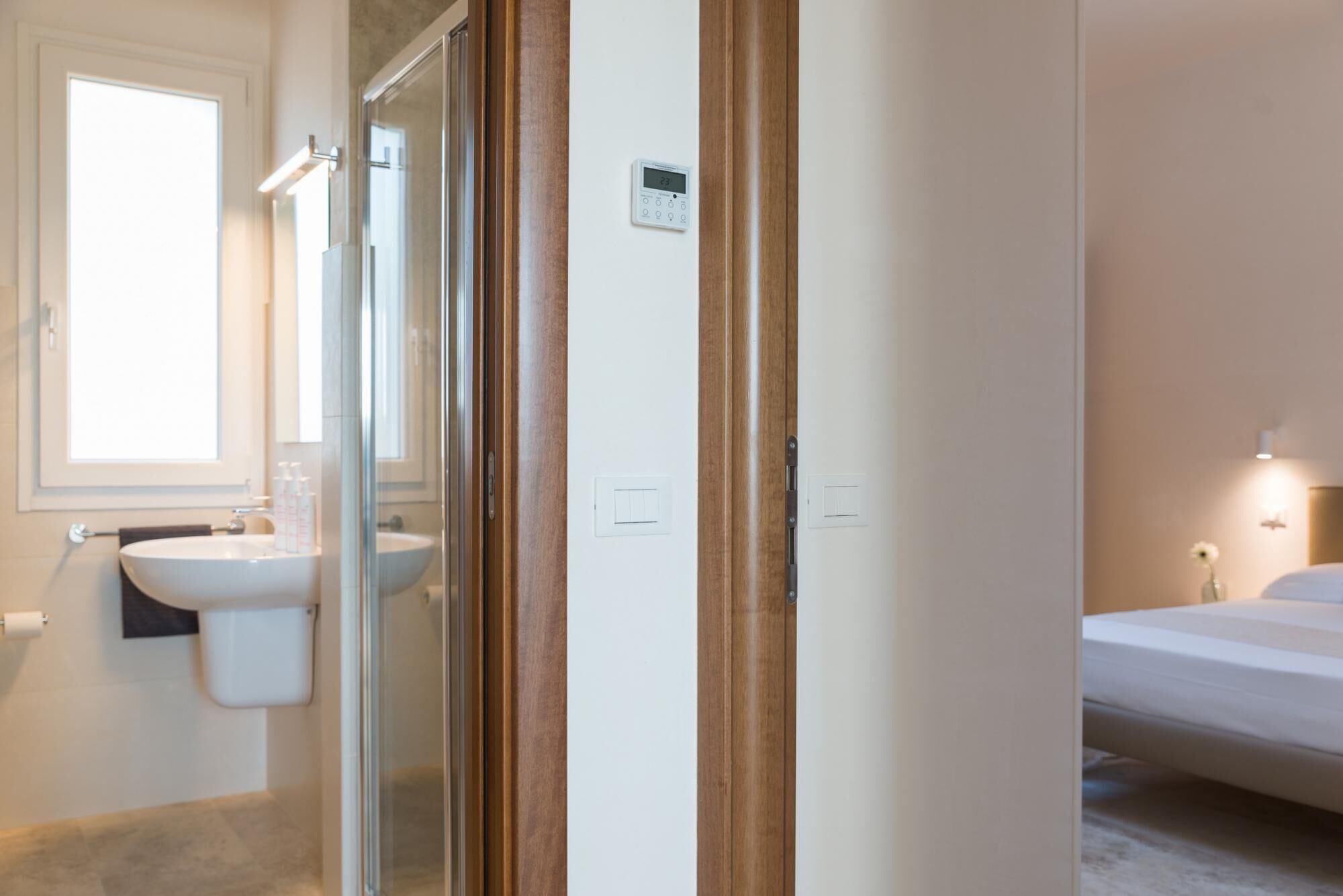 A bathroom with a glass shower enclosure, a sink, and a toilet. There is a wooden door with a digital lock and a small control panel above it.