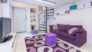 Ein modernes Wohnzimmer mit einem violetten Sofa, einem Flachbildfernseher, einer Wendeltreppe und einem Bücherregal.