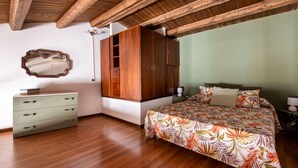 A bedroom with wooden flooring, a bed with a floral bedspread, a wardrobe, a dresser, and a mirror on the wall. - Casa Meli in Piazza S Domenico by Wonderful Italy (Palermo)