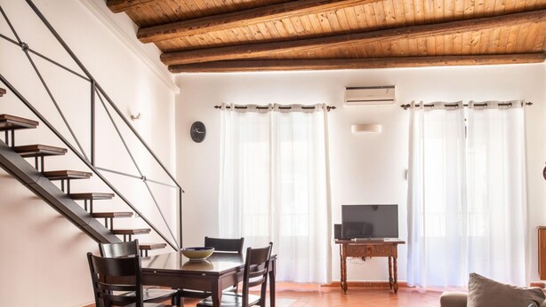 A living room with a wooden staircase, a dining table with chairs, a television on a stand, and a sofa. - Casa Meli in Piazza S Domenico by Wonderful Italy (Palermo)