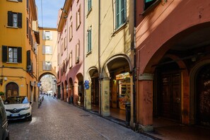 A cobblestone street lined with historic buildings, some with arches and signage. - Vista Sulle Torri di Bologna by Wonderful Italy (Bologna)