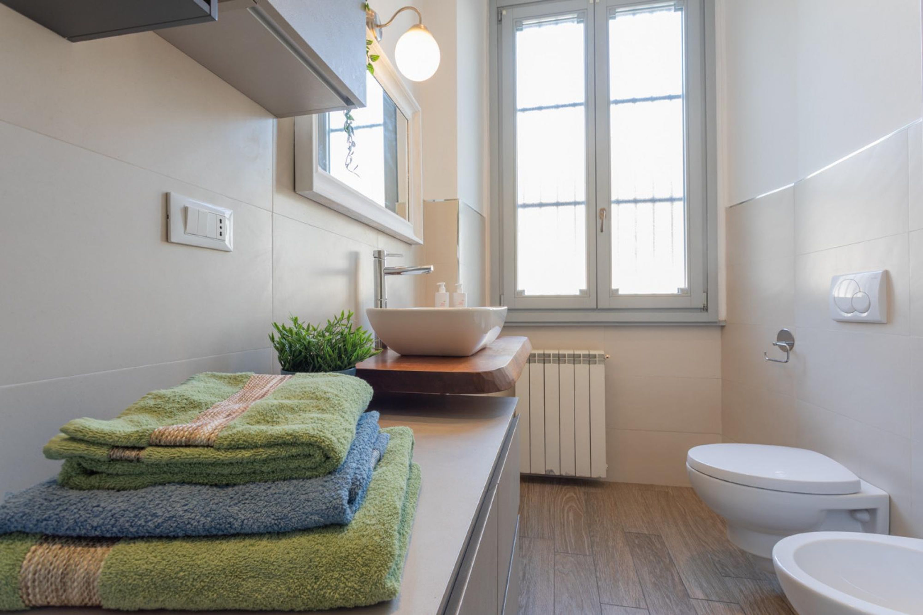 A modern bathroom with a white sink, a toilet, and a window providing natural light.