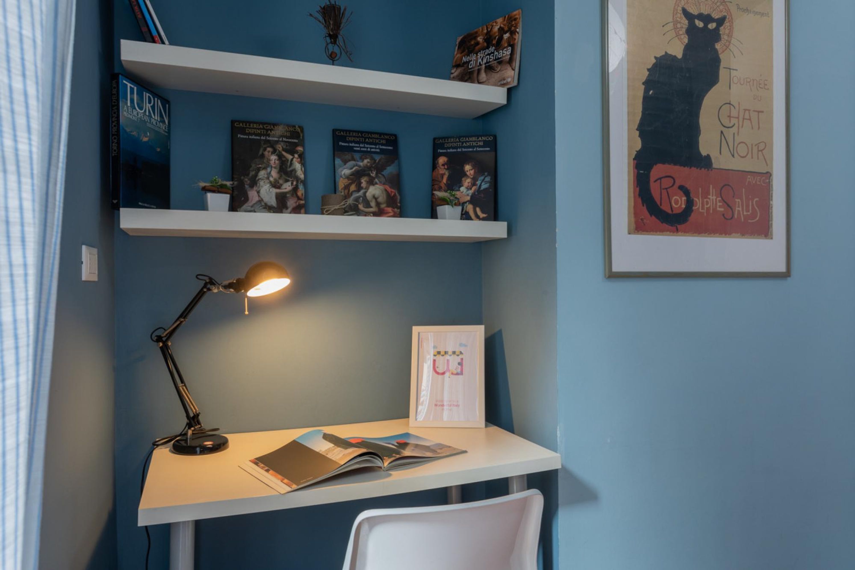 A study area with a desk, chair, shelves with books, and a framed poster on the wall.
