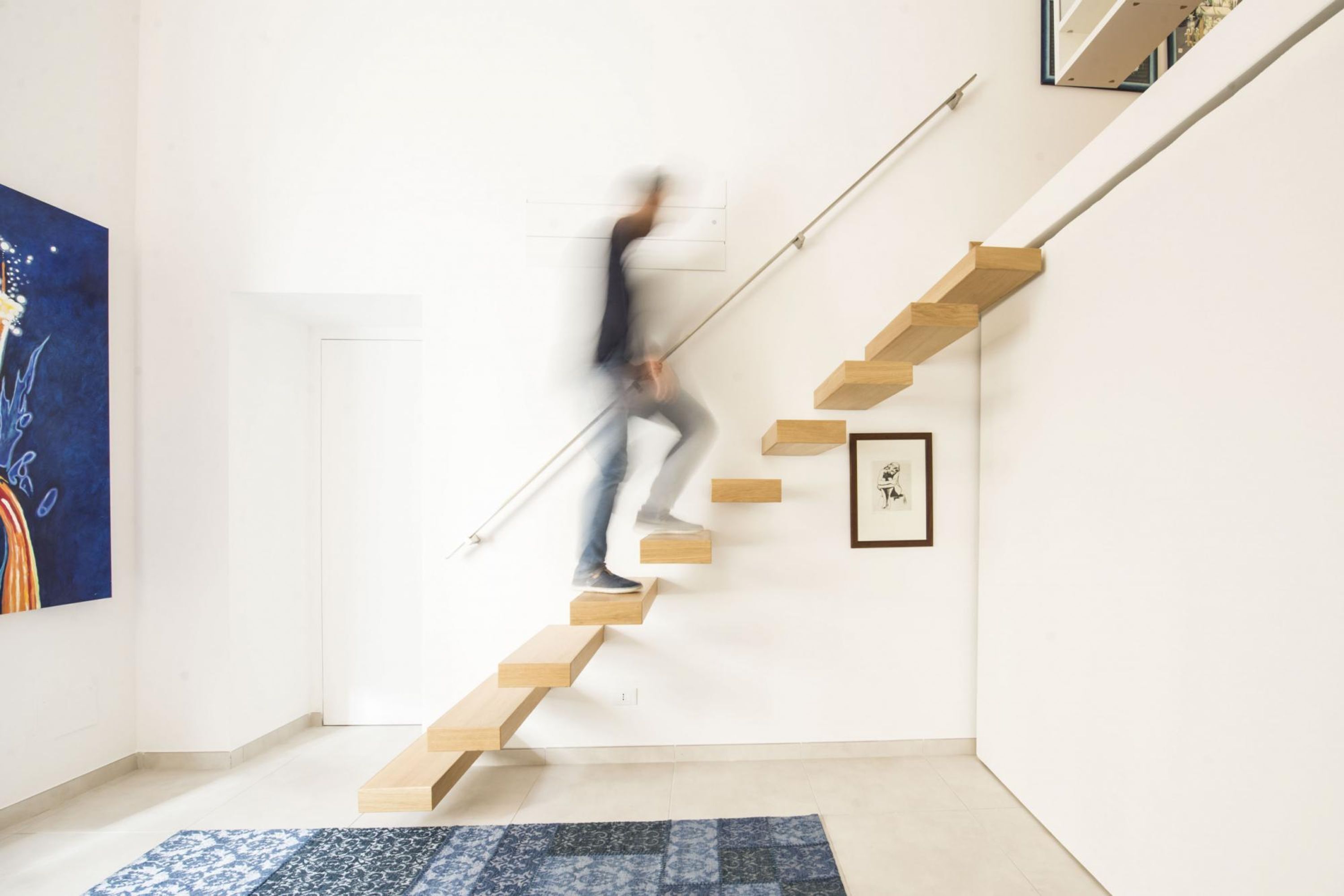 A modern interior with a wooden staircase, a framed artwork on the wall, and a patterned rug on the floor.