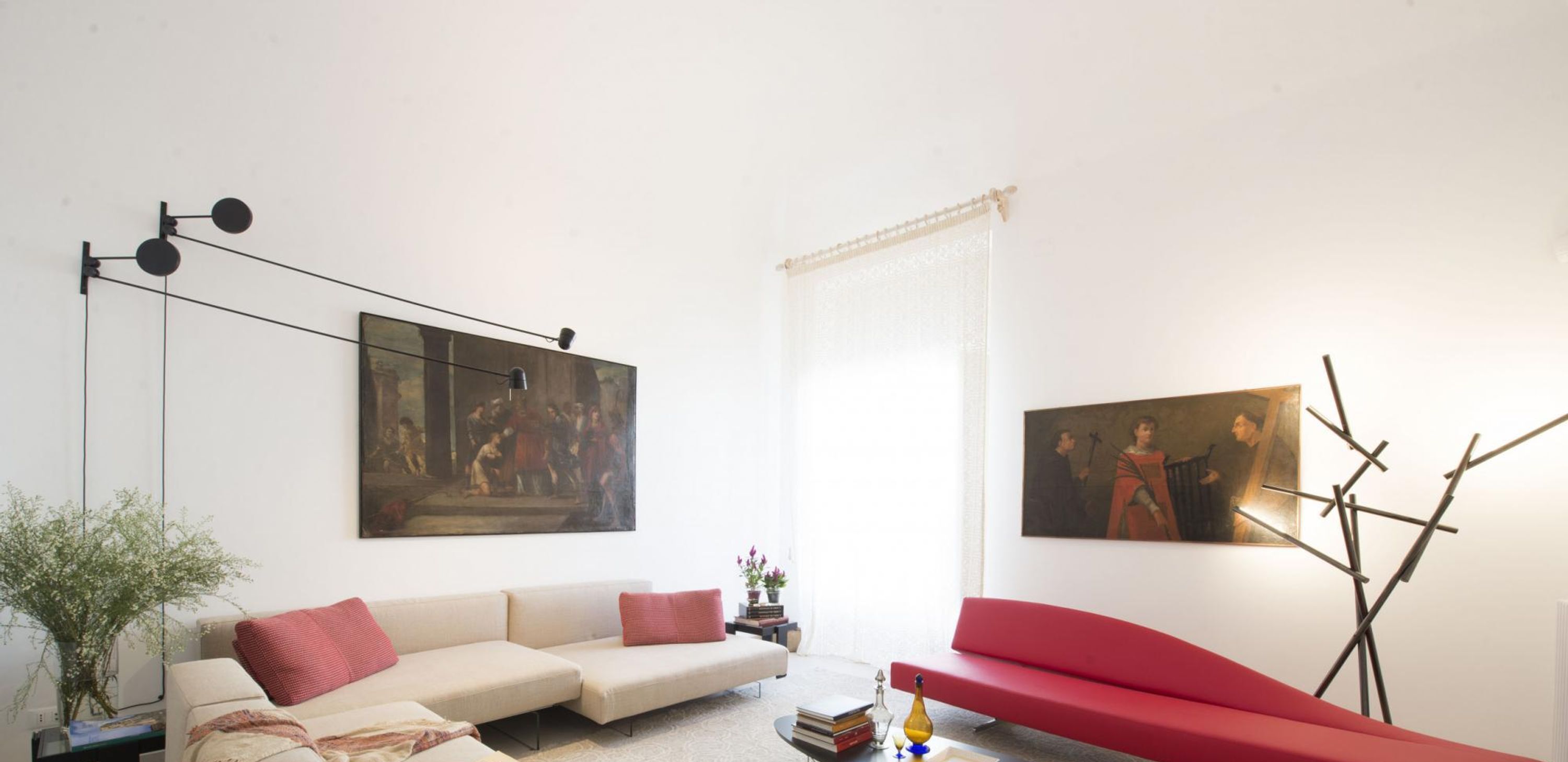 A living room with a beige sofa, a red armchair, and two paintings on the walls.