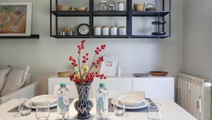 A dining area with a table set for four, a vase with red berries, and a shelf above with jars and baskets.