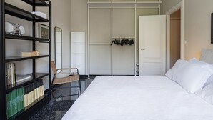 A bedroom with a bed, a bookshelf, a chair, a wardrobe, and a hanging rack.