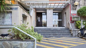 A building entrance with a covered staircase, a scooter parked outside, and a sign indicating a post office.