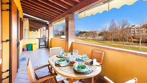 A balcony with a table set for dining, a view of the city, and a covered area with a door and trash bins.
