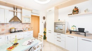 A modern kitchen with white cabinets, a gas stove, an oven, and a dining area with a glass table and chairs.