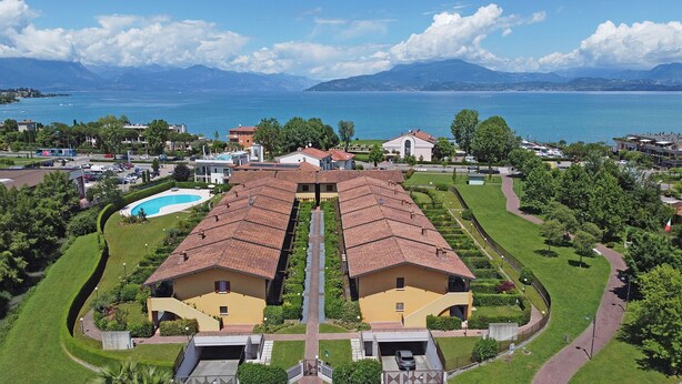 A large hotel with a central courtyard, multiple buildings, and a view of the sea and mountains in the background.