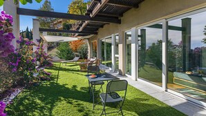 Een moderne patio met een tafel en stoelen, een pergola en uitzicht op de tuin via grote schuifdeuren.